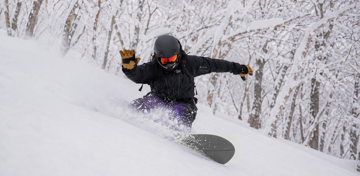 Snowboarder in MHD Backcountry Pro goggles with orange mirror lens, powder turn through trees
