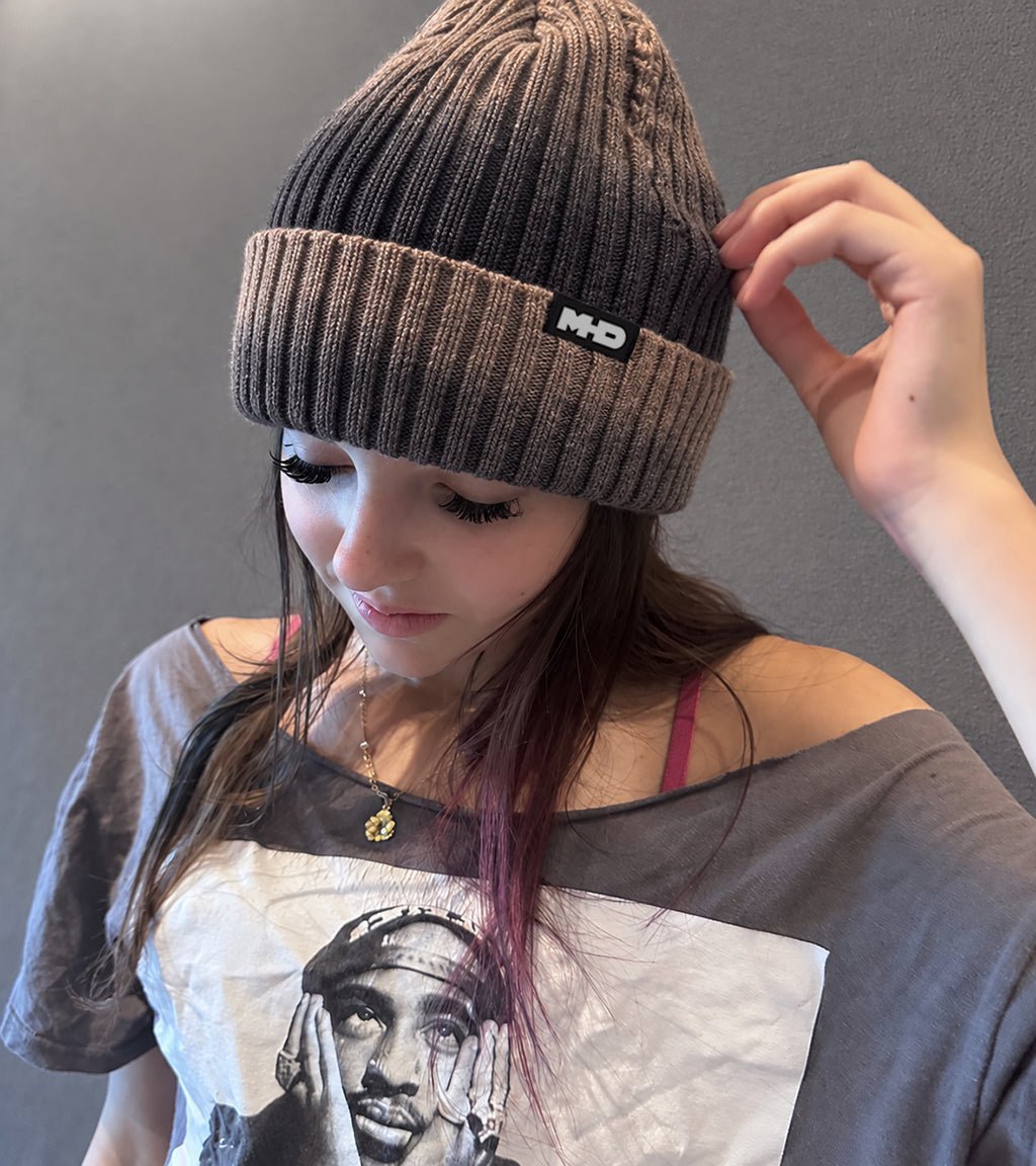 A person wearing a knit  dark grey and medium brown MHD Beanie