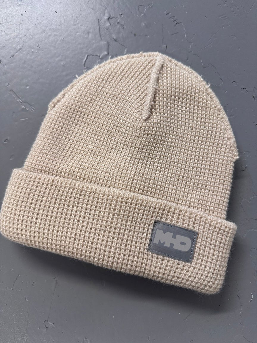 Sand snowboard beanie by MHD laid flat, with woven logo tab